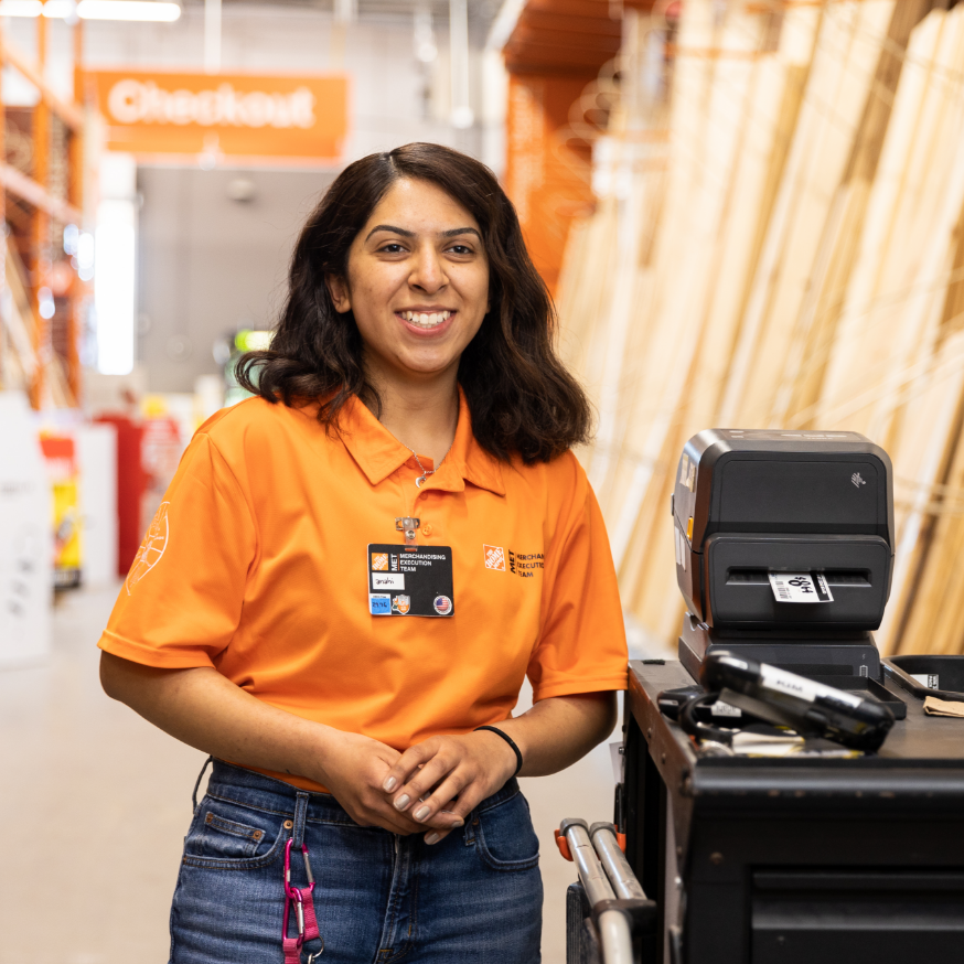 Hispanic female wearing orange polo shirt stands next to merchandising equipment.