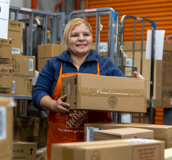 Hispanic female wearing orange apron carries cardboard box.