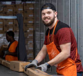 White male in black hat and orange apron works at a conveyor belt.