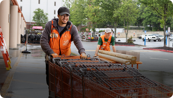 A man wearing an orange vest pushing carts in a Home Depot parking lot